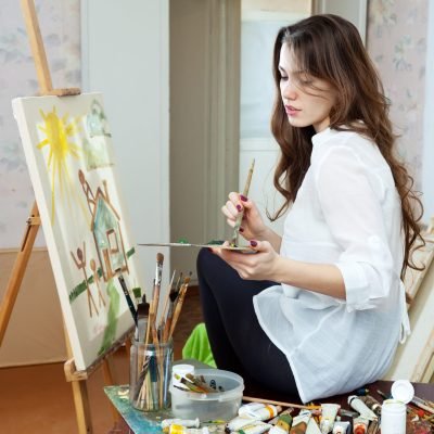 Yuong adult artist paints the house on canvas in studio